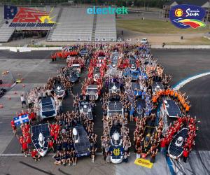Overhead group photo of dozens of collegiate solar car teams and their vehicles arranged across a speedway, everyone waving toward the camera. Logos for American Solar Challenge, electrek, and Formula Sun are overlaid at the top. A Quebec flag and multipl