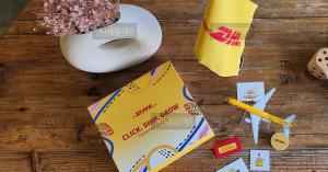 Yellow DHL-branded corporate gift box, desk flag, model airplane and promotional items arranged on a wooden table.