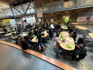 Large group of middle school students seated at round tables in a school gymnasium decorated with green and white balloons, participating in a Level Up program event.