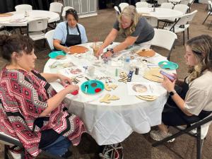 Women painting wooden door hangers around a white table at a Cornerstone Workshop door hanger crafting event