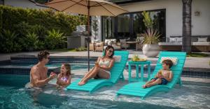 Family enjoying AquaCurve in-pool lounge chairs on a shallow sun shelf in a residential backyard pool.