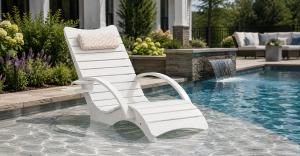 White AquaCurve in-pool lounge chair with armrests on a shallow sun shelf in a backyard pool.
