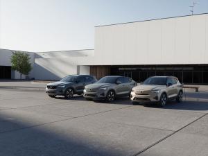 Drei SUVs der Volvo 40er-Reihe in Grau, Grün und Beige, geparkt vor einem modernen Showroom, eines an eine Ladestation angeschlossen.