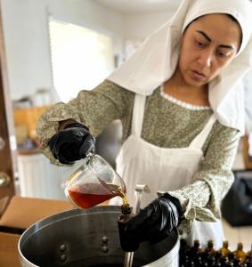 Sister Camilla in the kitchen in apron, with gloves, filling 2 oz oil bottles