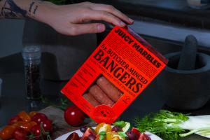 A pack of Juicy Marbles Butcher-minced Bangers teeters precariously above a succulent dish.