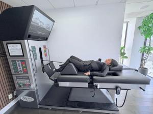 DRX9000 Spinal Decompression Table with Patient Laying on it being treated for low back pain. patient has harness holding upper body and another belt around the pelvic area. Patient looks comfortable and happy.