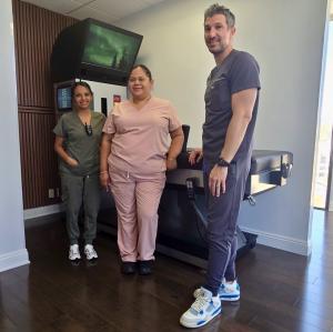 Dr. Nick Kousoulis standing with his staff in front of the the DRX9000 spinal decompression table.