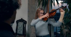 Emma with her arm in a cast holding a violin in a scene from The Concertmaster.