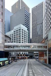 Street-level view of the Hong Kong central business and financial district, featuring modern high-rise corporate buildings, an elevated pedestrian walkway, and tram tracks.
