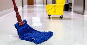 Blue commercial wet mop and yellow wringer bucket on a polished hard floor in an office building corridor