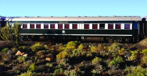 Side view of a green Pride of Africa carriage of Rovos Rail against Karoo scrubland