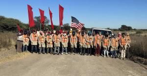 Flagging team in orange vests holding red flags and an American flag on a dirt road on South Africa's Highveld