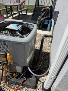 A Daikin outdoor air conditioning condenser unit next to a house, connected to professional yellow and blue digital manifold gauges for system testing.