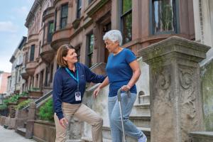 A female physical therapist from VNS Health helps an older patient down the stars