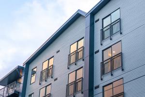 The Cartwright Apartments in daylight, a four-story building with pale blue-gray horizontal siding, black-railed balconies and warmly lit windows set against a cloudy evening sky.