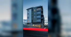 The Cartwright Apartments photographed at dusk from street level, a tall dark building with vertical CARTWRIGHT signage and lit ground-floor glass, with red car light trails streaking across the foreground.