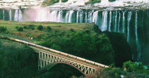 Rovos Rail Pride of Africa train crossing the steel arch bridge at Victoria Falls with the falls behind