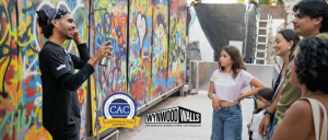 Artist explains his graffiti art on a vibrant wall to a family of four at Wynwood Walls street art museum.