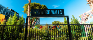 Entrance gate to Wynwood Walls outdoor art space with greenery and murals visible behind a black metal fence.
