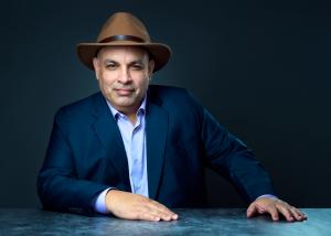 Portrait photo of Jonathane Ricci seated at a table, wearing a hat and navy blazer.