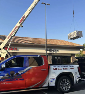 Mechanical Air branded service truck on-site as a crane lifts a commercial HVAC rooftop unit onto a building in the Central Valley.