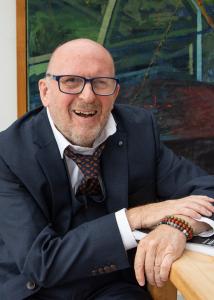 Author Anthony Peter Prior smiling while seated in a navy suit and patterned tie.