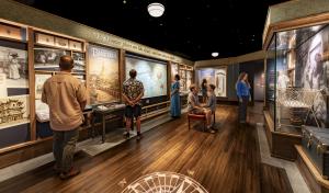 Museum visitors exploring the "Circle the Globe" gallery at the redesigned Herbert Hoover Presidential Library and Museum, featuring a world travel map, period travel posters, and artifacts from the Hoovers' journeys abroad.