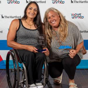 Cheri Madsen and Wendy Gumbert holding awards in front of a Move United backdrop