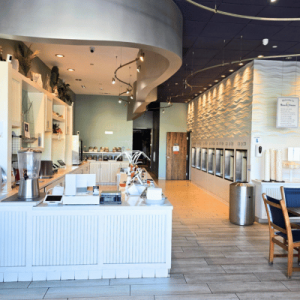 Modern, clean self-serve frozen yogurt shop with white counters, wall-mounted machines, and seating area with wooden chairs and tables.