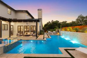 Twilight view of a Terrell Hills luxury home's backyard, featuring a resort-style pool, illuminated stone water feature, covered patio lounge, and fire pit.