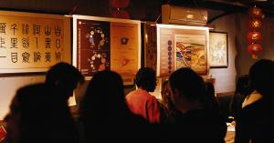 Guests gather beneath large data visualization posters displayed against a restaurant wall decorated with artwork and red lanterns.