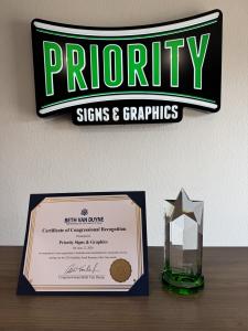 Priority Signs & Graphics logo displayed alongside the Congressional Recognition certificate and Southlake Small Business of the Year crystal award.