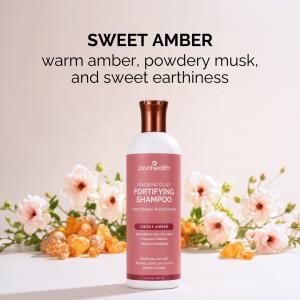 Zion Health Fortifying Shampoo centered against a soft blush background, surrounded by pale pink flowers and amber resin pieces representing its warm amber, powdery musk, and sweet earthy scent.