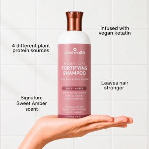 Zion Health Fortifying Shampoo balanced on an open hand against a white tiled background, with surrounding text highlighting four plant-protein sources, stronger-looking hair, vegan keratin, and the Sweet Amber scent.