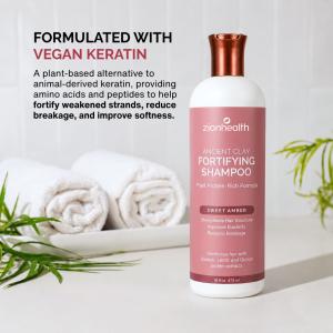 Zion Health Fortifying Shampoo displayed on a bright bathroom counter beside folded white towels and green plants, with text describing its revolutionary vegan-like keratin formula that mimics keratin benefits without animal-derived ingredients.