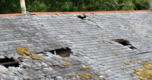 Slate roof with broken and missing tiles, moss growth, and open gaps exposing the roof deck