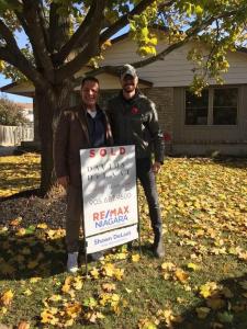 Shawn DeLaat standing with a sold sign at a Niagara home