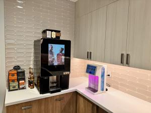 Bean-to-cup coffee brewer with a touchscreen display installed on an office breakroom counter, alongside a Bevi beverage dispenser, boxed tea selection, and flavored syrup bottles