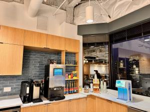Office breakroom coffee station with two commercial bean-to-cup brewers flanking a wooden mug rack, with cups, syrups, tea, and sweeteners arranged on the counter beneath a herringbone tile wall