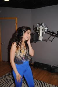Farrah Mechael recording vocals in a professional recording studio while wearing headphones.