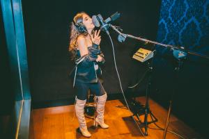 Farrah Mechael singing into a studio microphone during a vocal recording session.