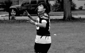 "Christopher Garcia looks up to catch a football during practice while wearing his football uniform."