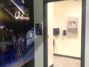 Aunt Flow free-vend period product dispenser mounted inside a women’s restroom at Huntington Park, with Columbus Clippers branding visible outside the restroom.