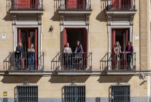 The team of Bacana Communications stands on three adjoining wrought-iron balconies of a classic Madrid building, with red-shuttered windows and a beige stone façade, on a sunny day in Spain. Title tag: Bacana Communications — Madrid, Spain Agency Office