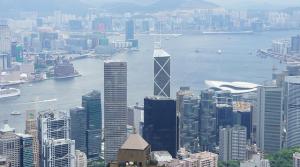A high-angle view of the Hong Kong skyline featuring prominent skyscrapers in the central business district overlooking Victoria Harbour.