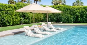 AquaCurve white pool loungers and matching side table arranged on a shallow backyard pool shelf under umbrellas.