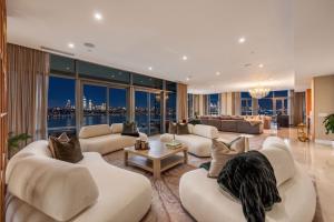 Furnished great room inside the 1000 Portside Drive penthouse in Edgewater, New Jersey, with floor-to-ceiling windows overlooking the Hudson River and illuminated Manhattan skyline.