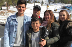 "Christopher Garcia stands with his family outdoors in front of a snowy mountain landscape."