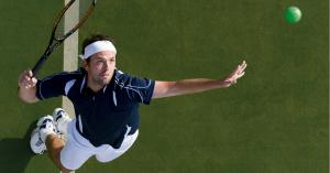 Tennis player reaching for the ball on a green court during an active match.