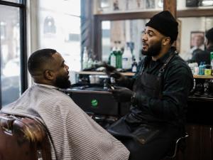 Local barber speaking with a customer inside a neighborhood barbershop connected to the Secret World creator community.